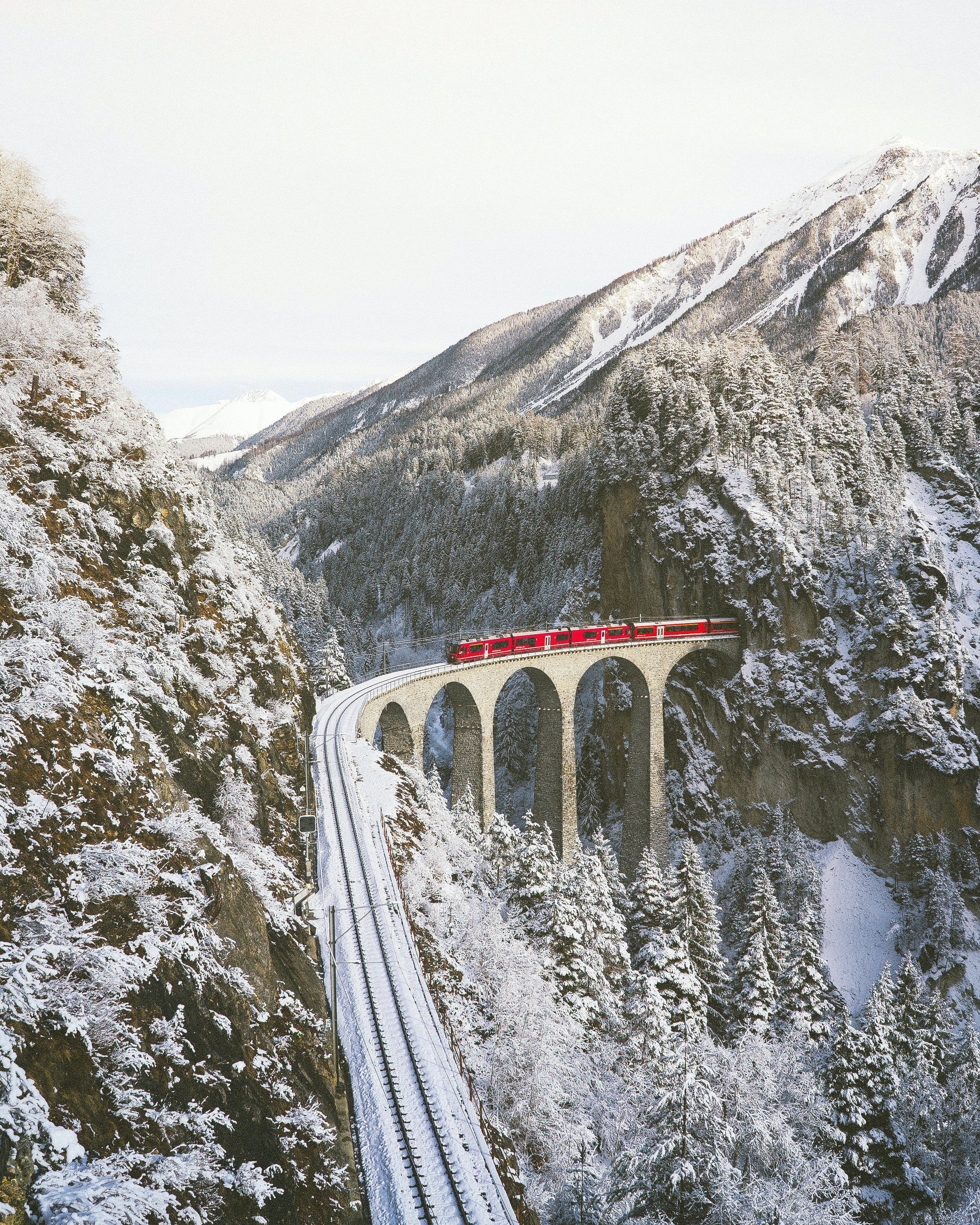 Paesaggio svizzero sotto la neve con un treno che passa sul viadotto in mezzo alle montagne. Foto di Johannes Hofmann