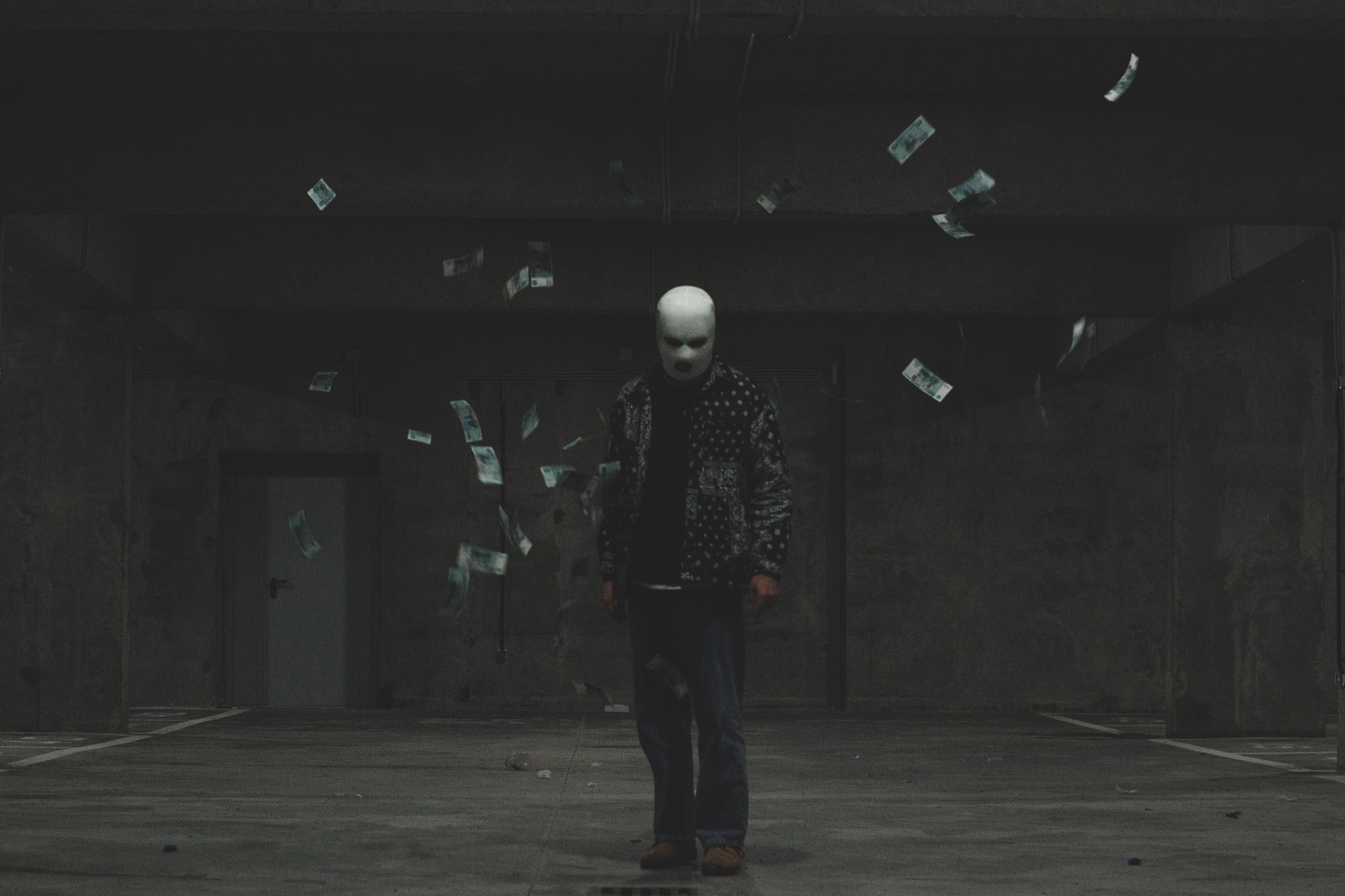 Hooded criminal surrounded by bills falling from above. Photo by Nikita Pavlov